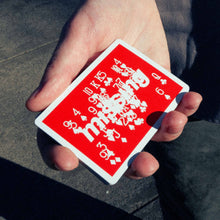 Load image into Gallery viewer, Hand holding a red playing card with white text and symbols on a concrete surface.
